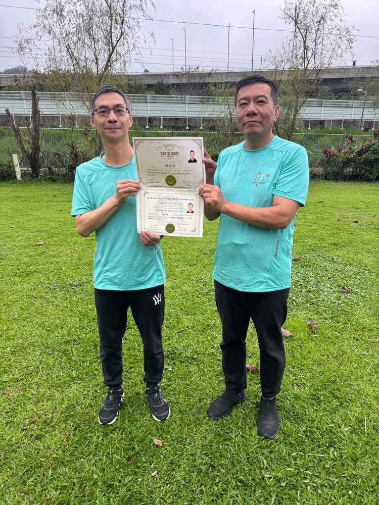 兩位穿著湖水綠色制服的學員和導師，在草地上一同展示高級系統訓練畢業證書
