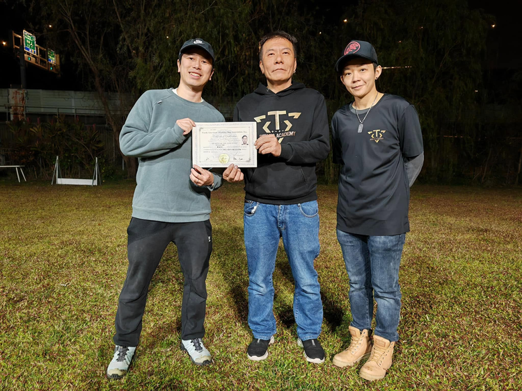學員手持證書，與兩位導師在訓練場合照