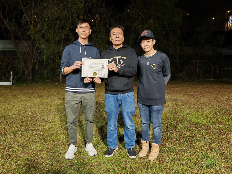 學員手持證書，與兩位導師在訓練場合照